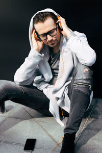 Young man looking away while sitting on black background