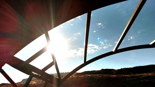 Low angle view of sun shining over landscape against sky