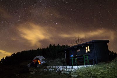 People camping by house against star field