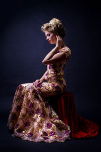 Side view of woman in evening gown sitting against black background