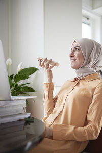 Smiling woman with hijab have conversation with colleague or friend on speaker mode