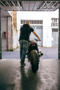 Rear view of man walking with motorcycle from garage