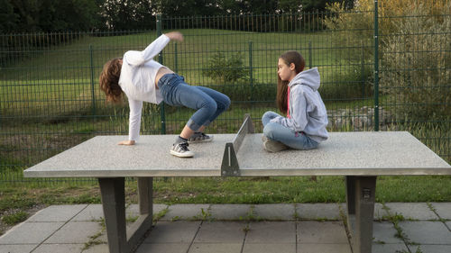 Girls sitting on table tennis table at yard