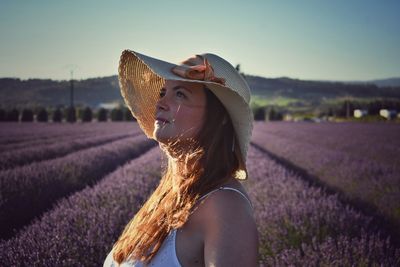 Side view of woman wearing hat standing on field against sky