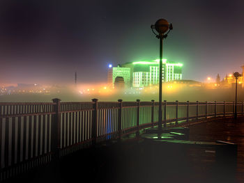 Illuminated street lights by bridge against sky at night