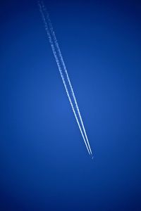 Low angle view of aircraft vapor trail against clear blue sky