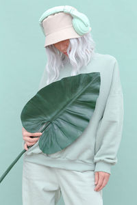 Full length of woman holding leaf while standing over green background