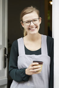 Portrait of smiling female owner having coffee at entrance of art studio