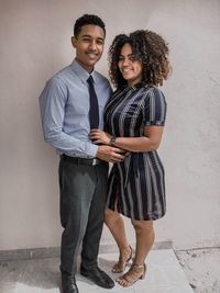 Portrait of a smiling young couple standing against wall