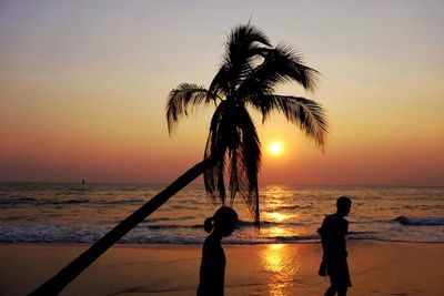 Silhouette people walking on beach at sunset