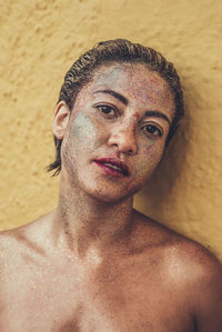 Portrait of topless mid adult woman with glitter on face standing against wall