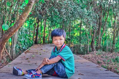 Portrait of boy sitting on plants against trees