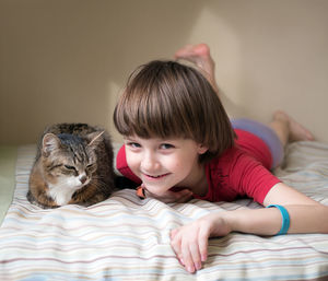 Portrait of boy with cat relaxing on bed at home