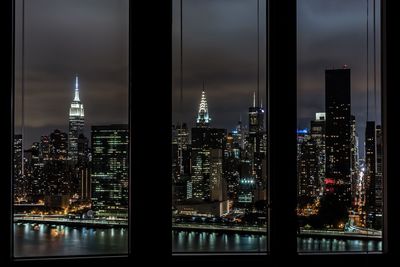 Empire state building amidst illuminated towers seen through window