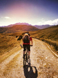 Rear view of man riding bicycle on mountain against sky