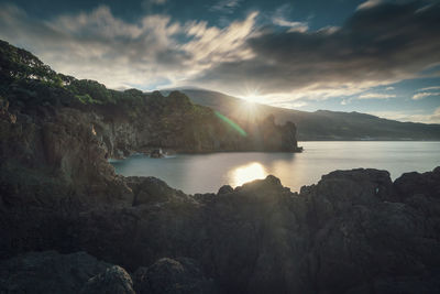 Rocks by sea against sky during sunset