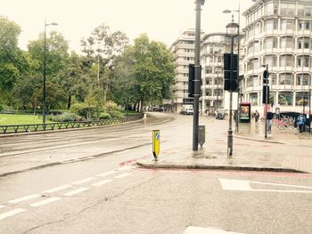 Road by trees and buildings against sky