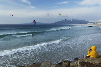 Scenic view of wind surfers at sea against cloudy sky