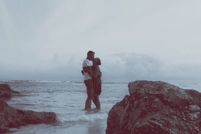 Couple kissing while standing in sea against sky