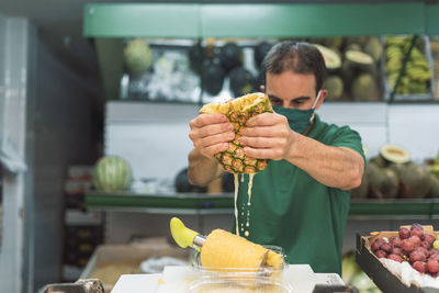 A man squeezing a pineapple in his own fruit shop