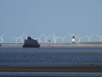 Traditional windmill by sea against clear blue sky