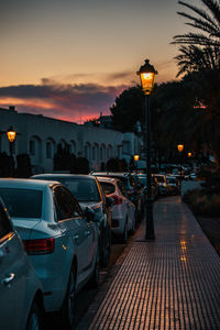 Cars on street by buildings against sky at sunset