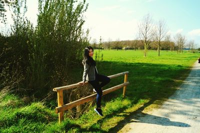 Young woman sitting on wooden fence on field