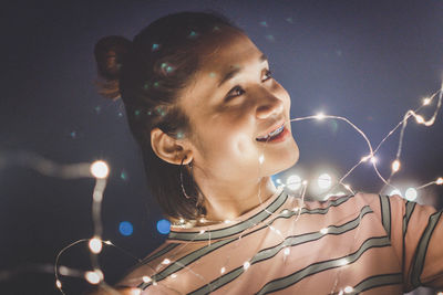 Smiling woman with illuminated string lights at home