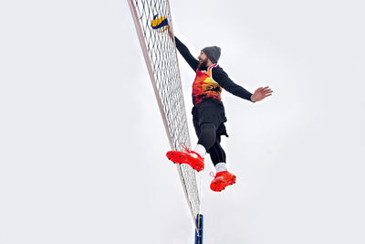 Man jumping by volleyball net against clear sky