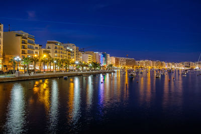 Illuminated buildings by river against sky at night
