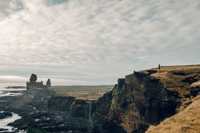 Scenic view of cliff against cloudy sky during sunset