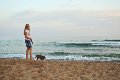 Girl with dog at beach against sky