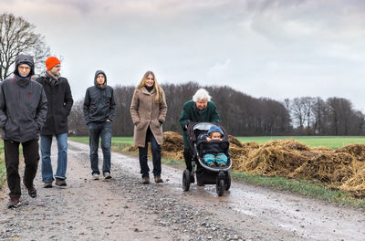 Family walking on dirt road against sky