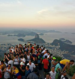 Crowd at corcovado mountain by sea against sky during sunset