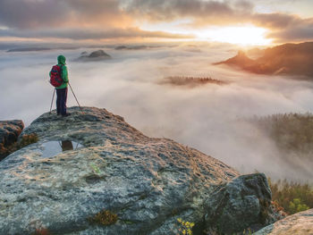 Man standing on rock against sky during sunset