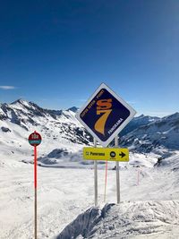 Road sign on snow covered mountain against sky