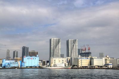 View of city at waterfront against cloudy sky