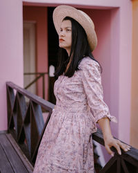 Portrait of woman wearing hat standing against railing