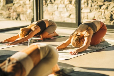 Women practicing child's pose on exercise mat during yoga class at retreat center