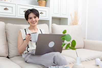 Young woman using laptop while sitting on sofa at home