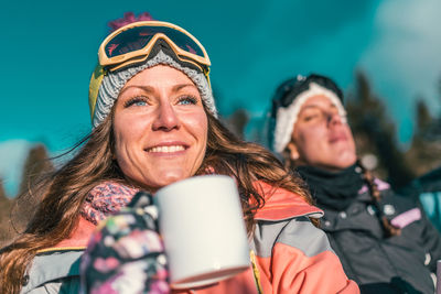 Woman having coffee with friend against sky in sunny day