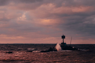 Lighthouse by sea against sky during sunset