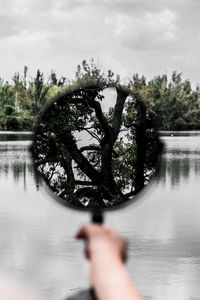 Person holding tree by lake against sky