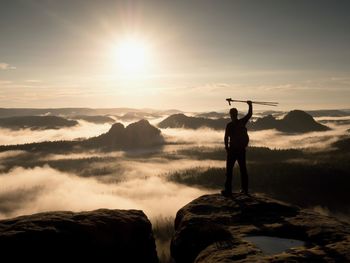 Hiker on peak. tourist man on peak with trekking poles in hand raised in air. marvelous daybreak