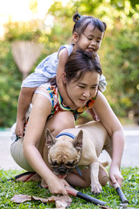 Mother piggybacking daughter while playing with pug outdoors