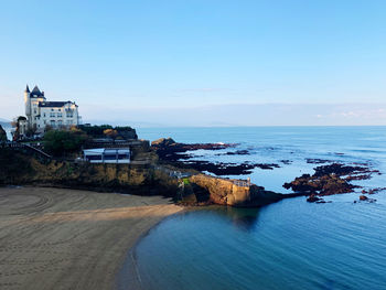 Scenic view of sea by buildings against clear blue sky