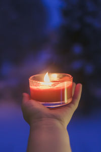Burning red candle in a hand on winter background