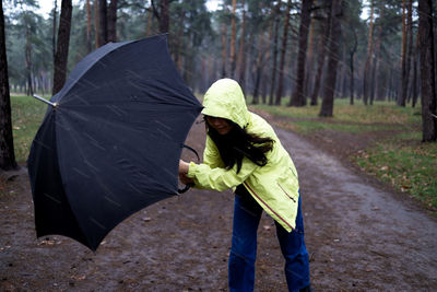 Woman trying to hold her umbrella in strong wind in forest.