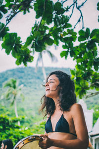 Young woman looking away while standing against tree