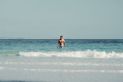 Full length of shirtless man in sea against sky